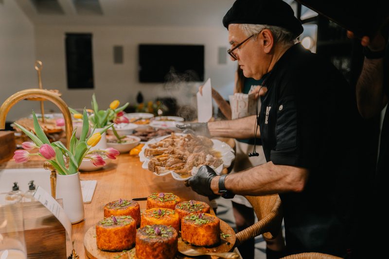 Chef Reza carrying a steaming platter at a catered event